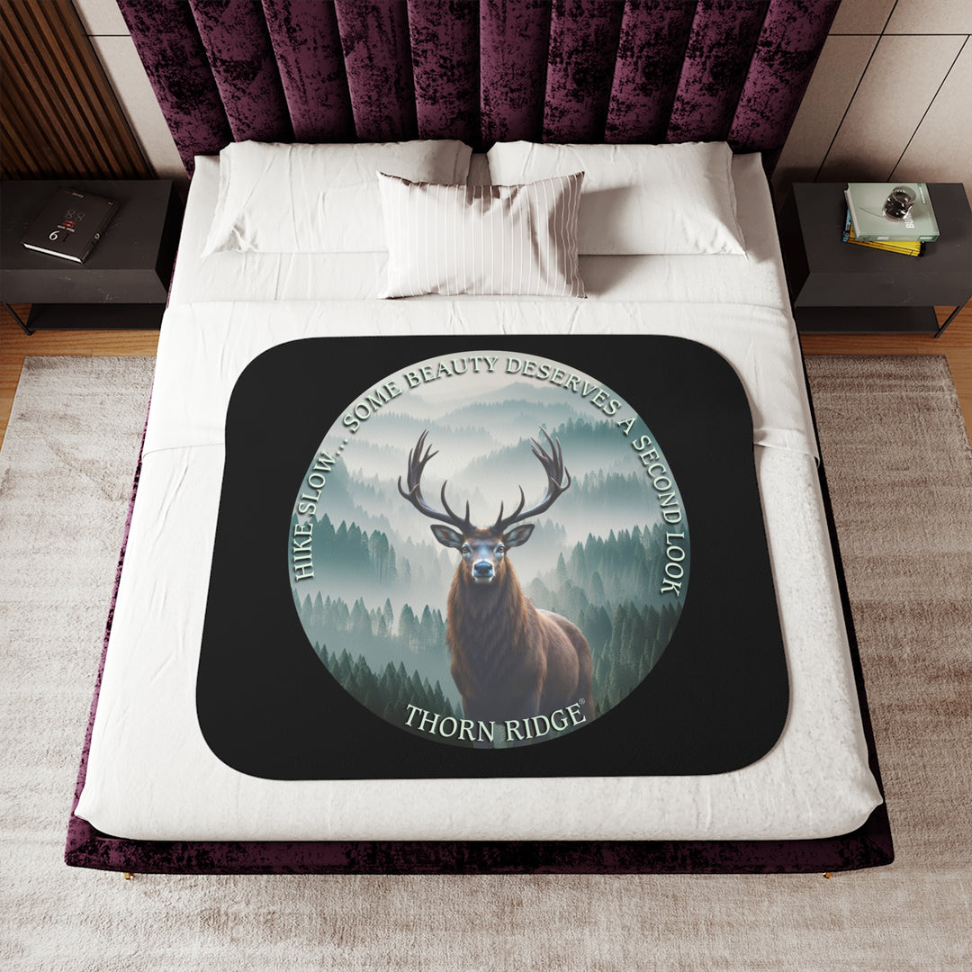 Hike Slow some beauty deserves a second look black sherpa blanket featuring a circular graphic of a buck looking at the camera with a green misty forest behind him and branded Thorn Ridge®