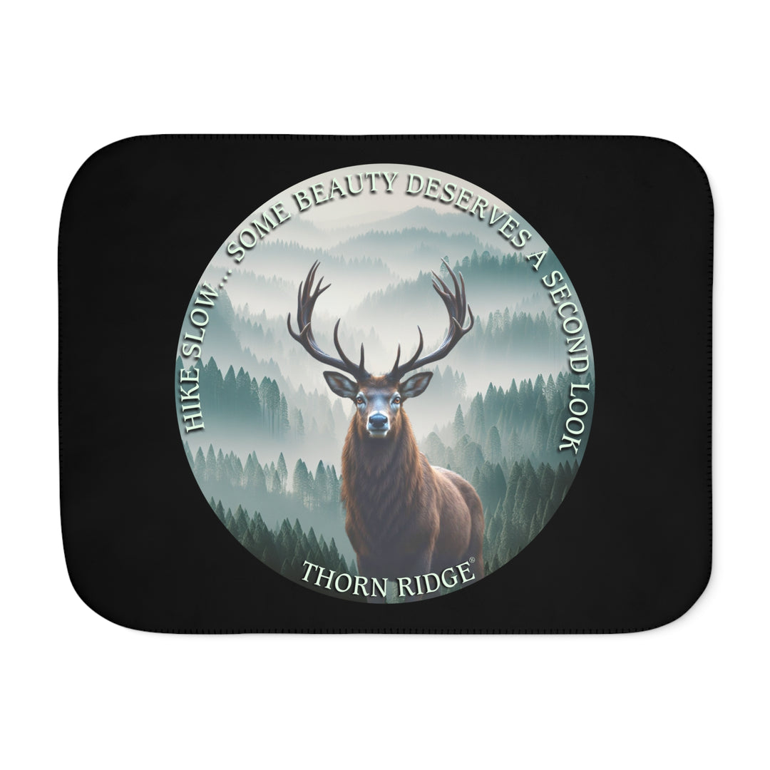 Hike Slow some beauty deserves a second look black sherpa blanket featuring a circular graphic of a buck looking at the camera with a green misty forest behind him and branded Thorn Ridge®