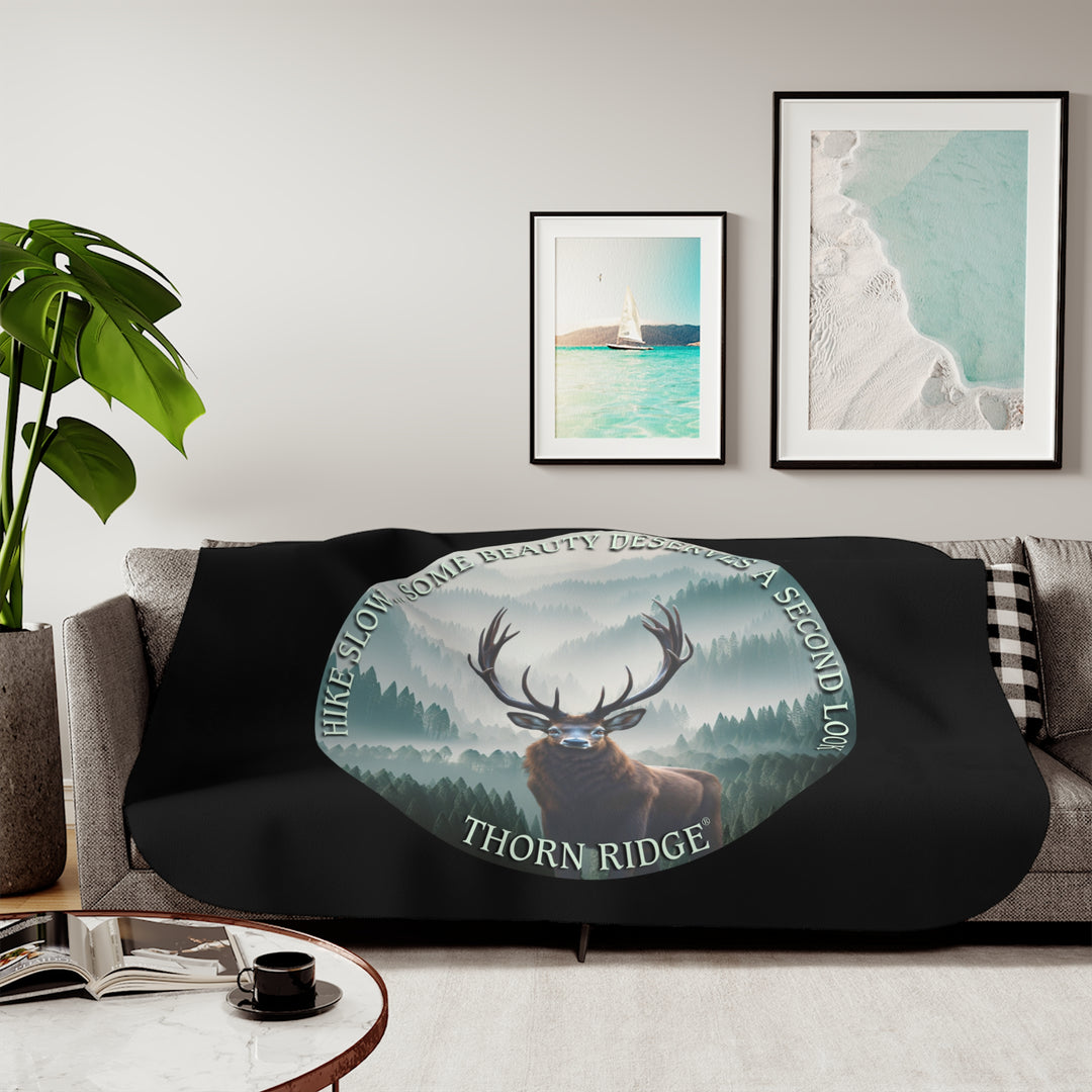 Hike Slow some beauty deserves a second look black sherpa blanket featuring a circular graphic of a buck looking at the camera with a green misty forest behind him and branded Thorn Ridge®