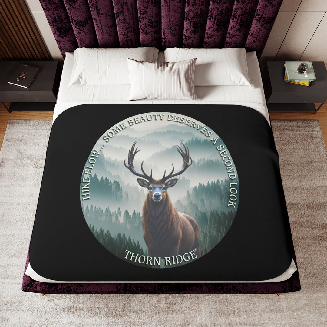 Hike Slow some beauty deserves a second look black sherpa blanket featuring a circular graphic of a buck looking at the camera with a green misty forest behind him and branded Thorn Ridge®