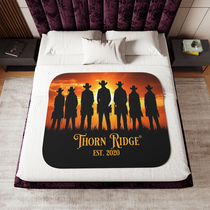 Silhouette of Seven Riders cowboys against an orange sunset with 'Thorn Ridge' branding on a sherpa blanket on a bed.