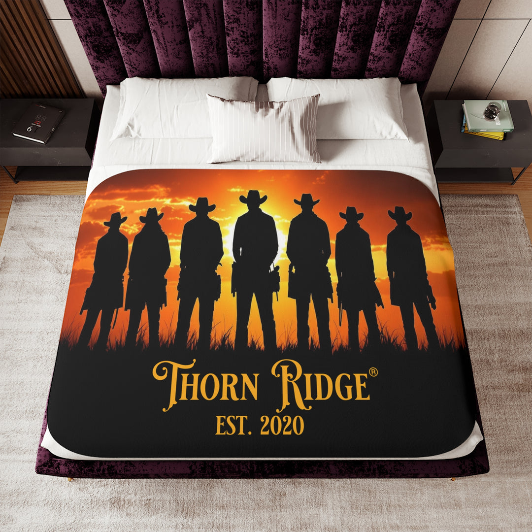 Silhouette of Seven Riders cowboys against an orange sunset with 'Thorn Ridge' branding on a sherpa blanket on a bed