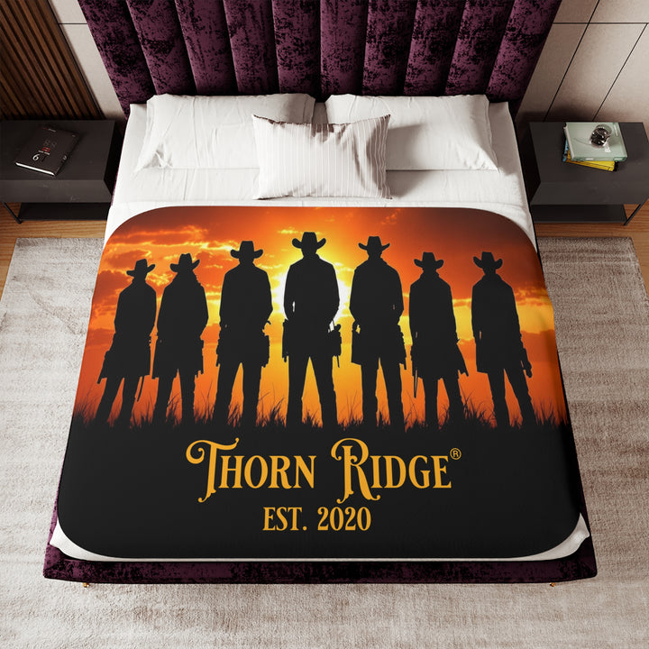 Silhouette of Seven Riders cowboys against an orange sunset with 'Thorn Ridge' branding on a sherpa blanket on a bed