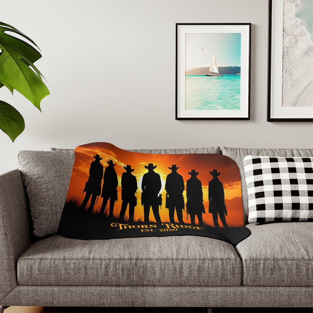 Silhouette of Seven Riders cowboys against an orange sunset with 'Thorn Ridge' branding on a sherpa blanket across a couch.