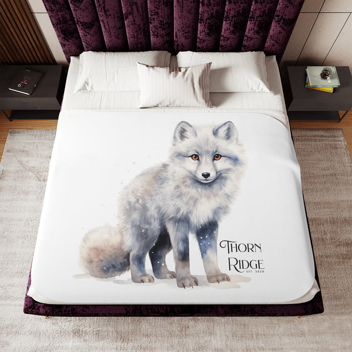White Arctic fox illustration on a white Sherpa Blanket with 'Thorn Ridge' branding and the blanket is laying across a bed. 