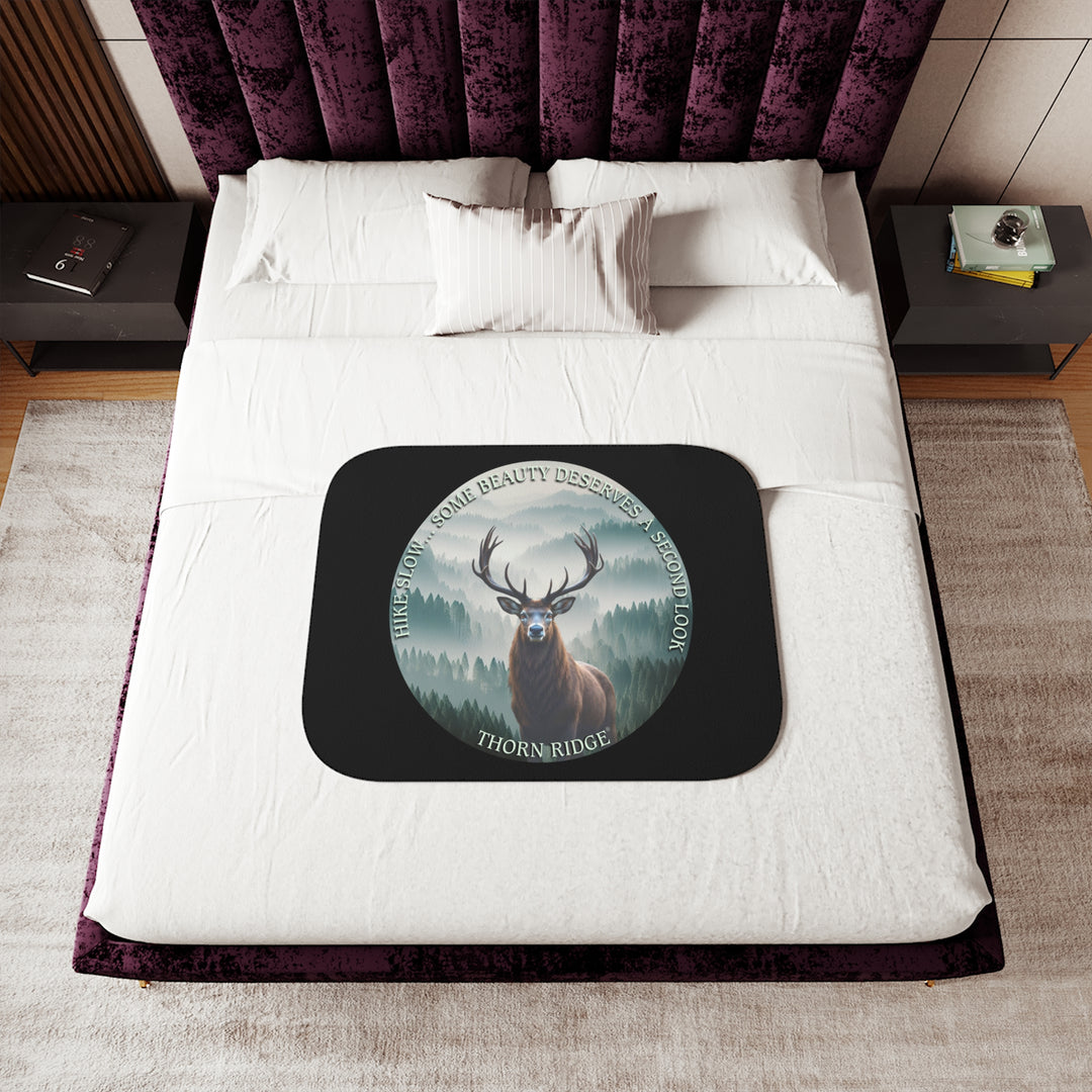Hike Slow some beauty deserves a second look black sherpa blanket featuring a circular graphic of a buck looking at the camera with a green misty forest behind him and branded Thorn Ridge®
