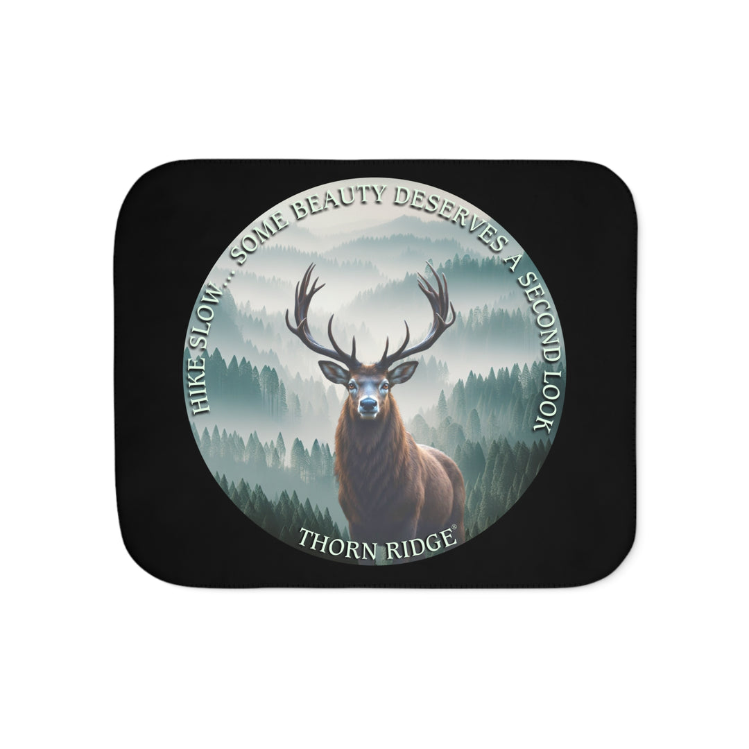 Hike Slow some beauty deserves a second look black sherpa blanket featuring a circular graphic of a buck looking at the camera with a green misty forest behind him and branded Thorn Ridge®