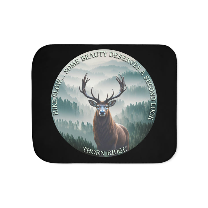 Hike Slow some beauty deserves a second look black sherpa blanket featuring a circular graphic of a buck looking at the camera with a green misty forest behind him and branded Thorn Ridge®