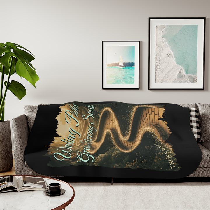 Winding Paths Grow Strong Souls black sherpa blanket with an image of a winding golden brick path through a forest with lights on top of the bricks that edge the path. By Thorn Ridge®