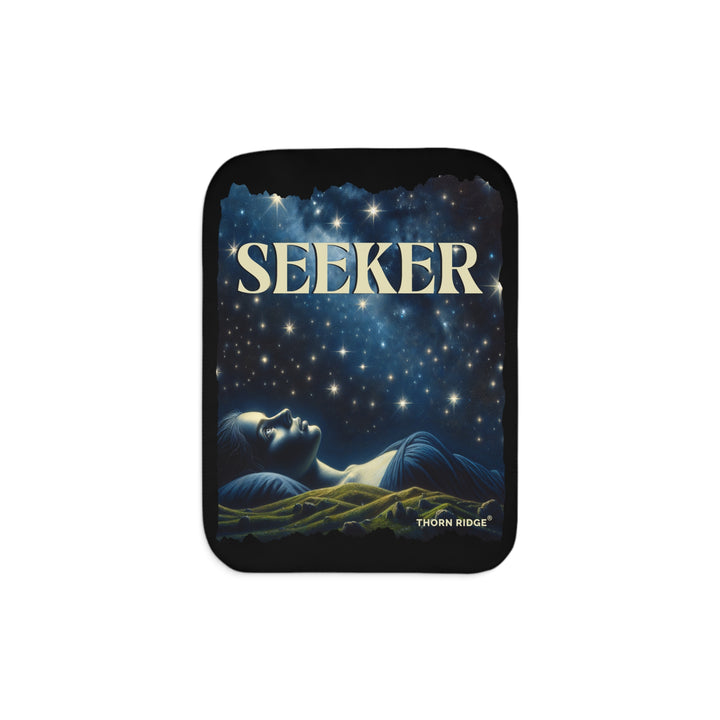 Seeker sherpa blanket in blacks and blues featuring the night sky and a woman laying on the ground stargazing. Branded Thorn Ridge®