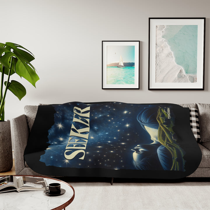 Seeker sherpa blanket in blacks and blues featuring the night sky and a woman laying on the ground stargazing. Branded Thorn Ridge®