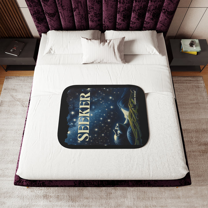 Seeker sherpa blanket in blacks and blues featuring the night sky and a woman laying on the ground stargazing. Branded Thorn Ridge®
