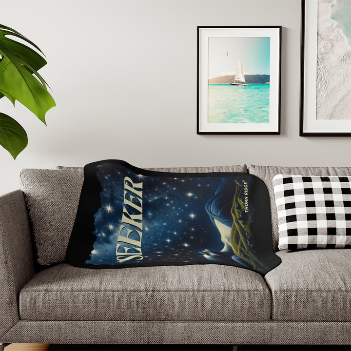 Seeker sherpa blanket in blacks and blues featuring the night sky and a woman laying on the ground stargazing. Branded Thorn Ridge®