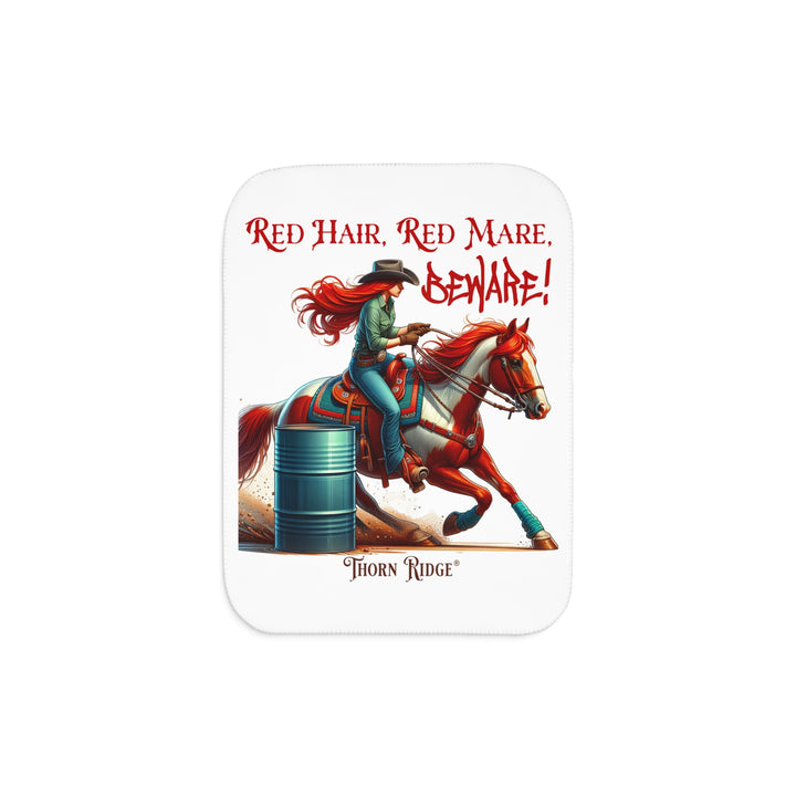 white sherpa blanket with a graphic of a redheaded woman on a tobiano  chestnut horse racing around a barrel and text 'Red Hair, Red Mare, Beware!' by Thorn Ridge®.
