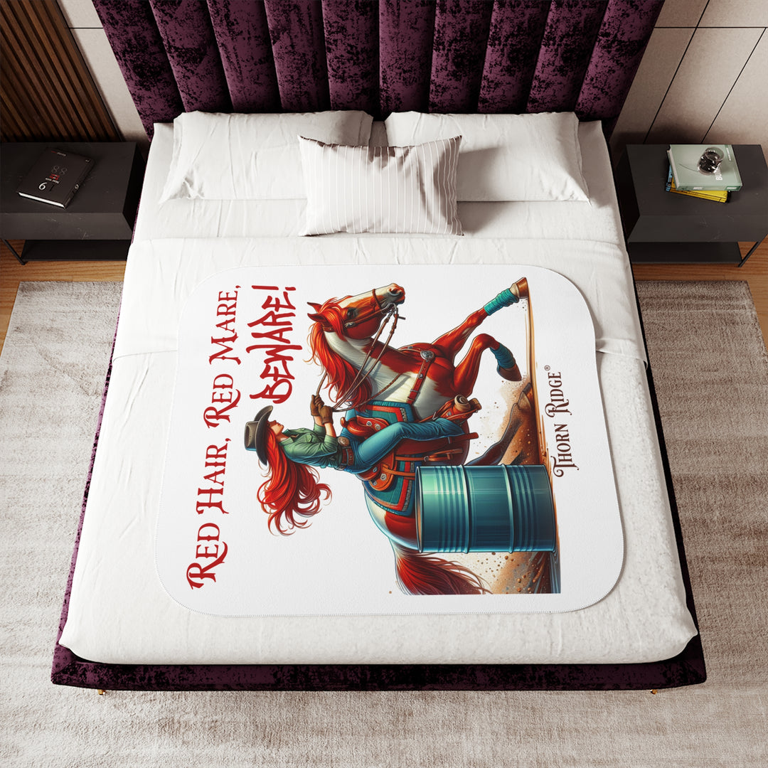white sherpa blanket with a graphic of a redheaded woman on a tobiano  chestnut horse racing around a barrel and text 'Red Hair, Red Mare, Beware!' by Thorn Ridge®.