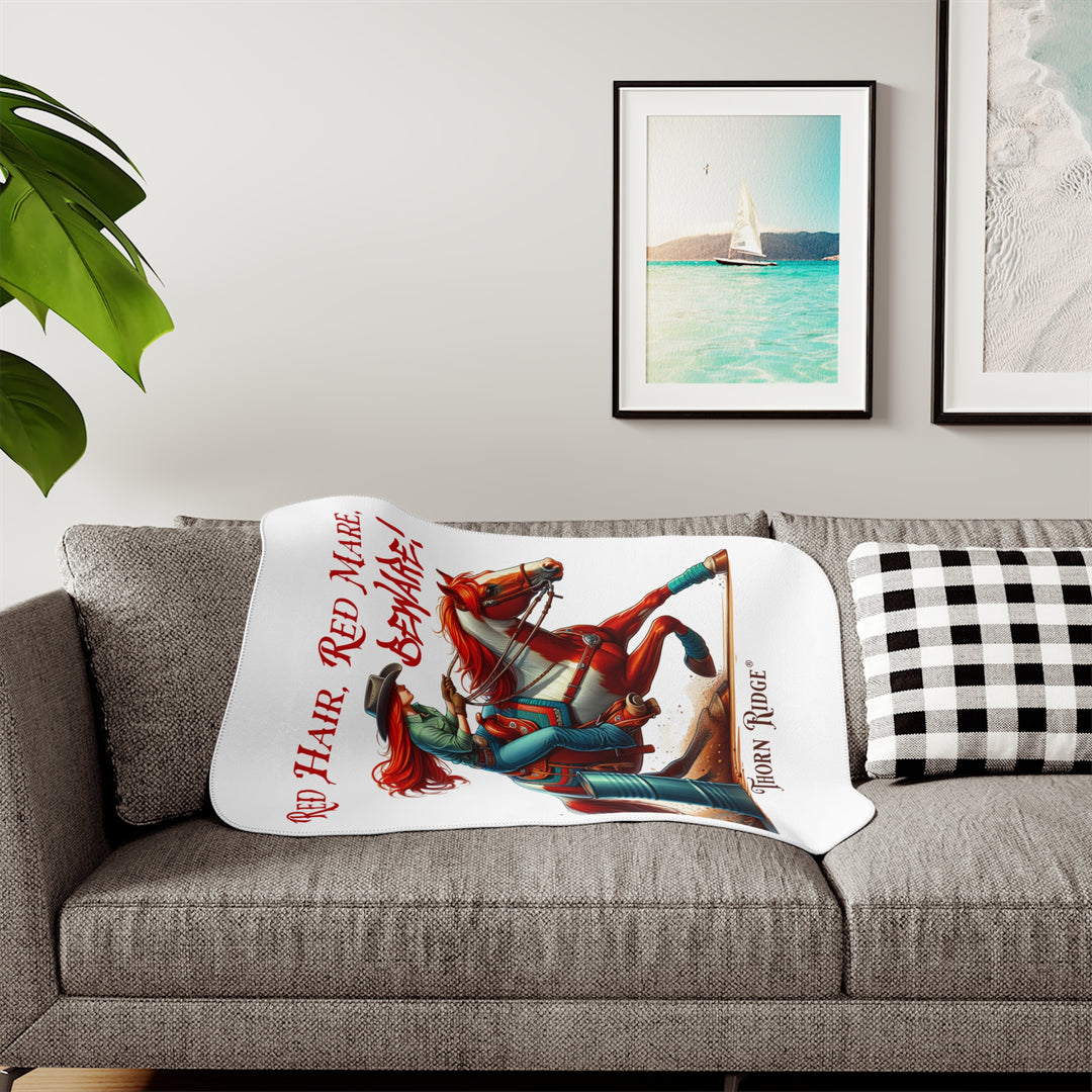 white sherpa blanket with a graphic of a redheaded woman on a tobiano  chestnut horse racing around a barrel and text 'Red Hair, Red Mare, Beware!' by Thorn Ridge®.