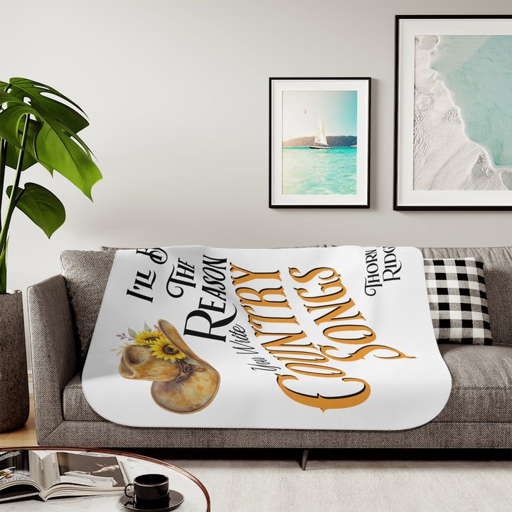 Decorative white sherpa blanket with a yellow sunflower cowgirl hat, sunflower, and text 'I'll be the reason you write country songs' by Thorn Ridge®