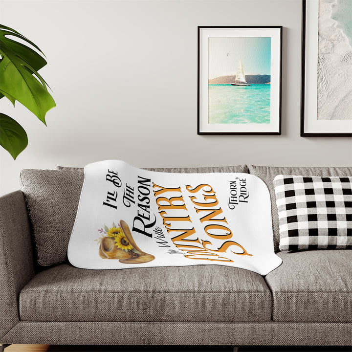 Decorative white sherpa blanket with a yellow sunflower cowgirl hat, sunflower, and text 'I'll be the reason you write country songs' by Thorn Ridge®