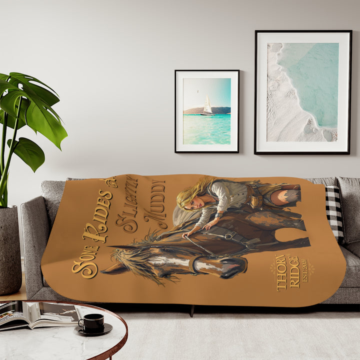 Some Rides Are Slightly Muddy tan sherpa blanket with an illustration of a draft horse in tack and a blond woman walking beside it both covered in mud and branded Thorn Ridge® EST 2020.