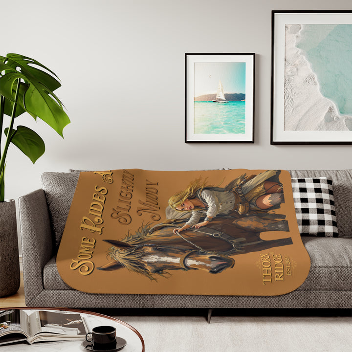 Some Rides Are Slightly Muddy tan sherpa blanket with an illustration of a draft horse in tack and a blond woman walking beside it both covered in mud and branded Thorn Ridge® EST 2020.