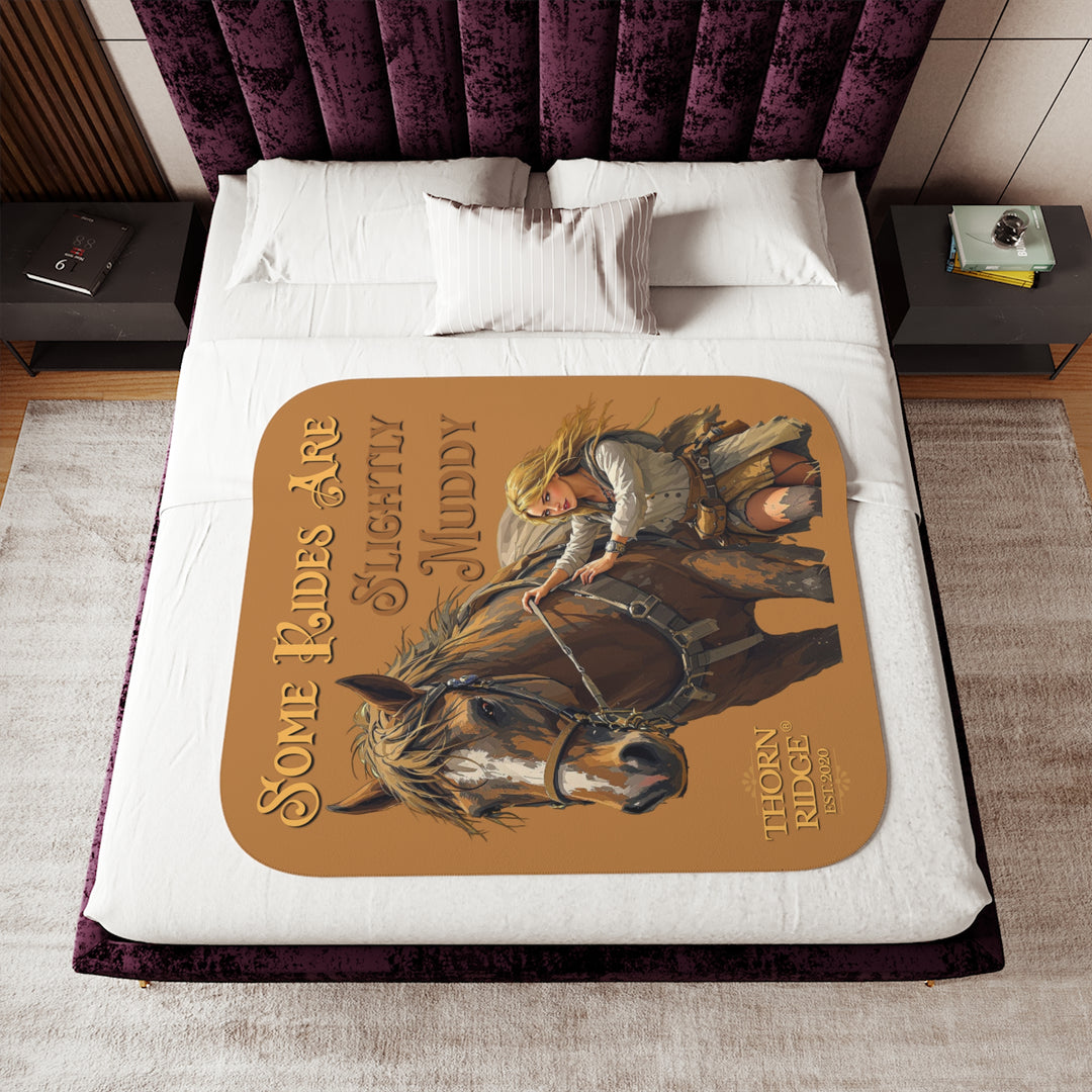Some Rides Are Slightly Muddy tan sherpa blanket with an illustration of a draft horse in tack and a blond woman walking beside it both covered in mud and branded Thorn Ridge® EST 2020.