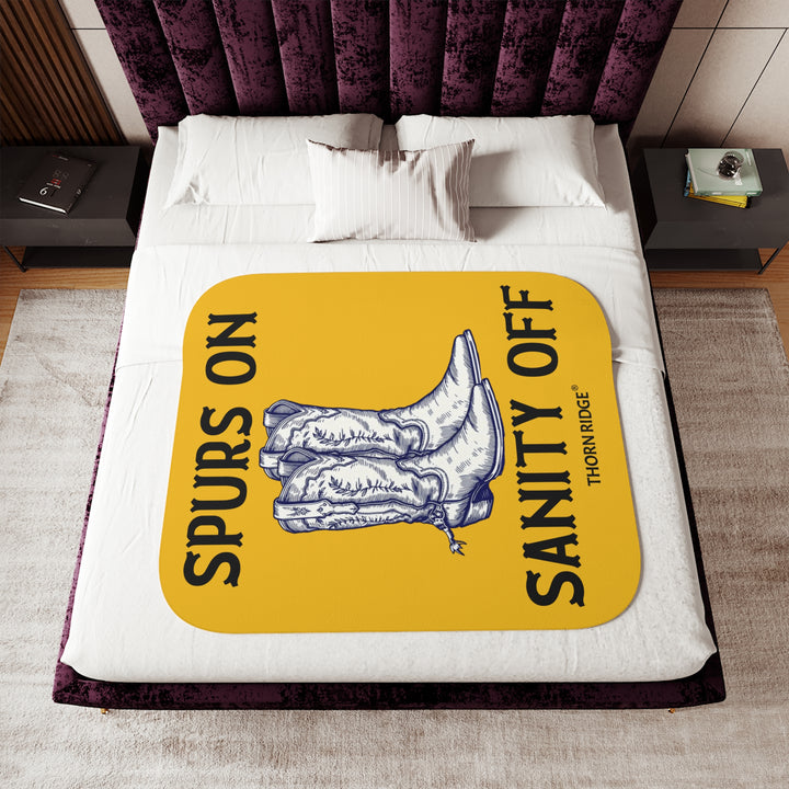 Spurs On Sanity Off yellow sherpa blanket with an illustration of white cowboy boots with spurs in the middle and branding Thorn Ridge®