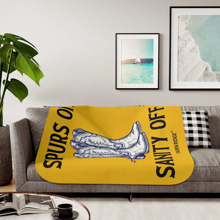 Spurs On Sanity Off yellow sherpa blanket with an illustration of white cowboy boots with spurs in the middle and branding Thorn Ridge®