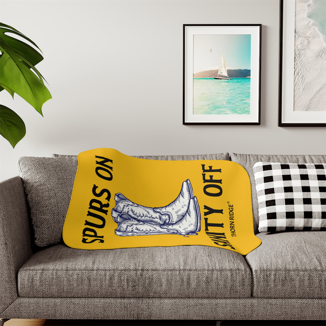 Spurs On Sanity Off yellow sherpa blanket with an illustration of white cowboy boots with spurs in the middle and branding Thorn Ridge®