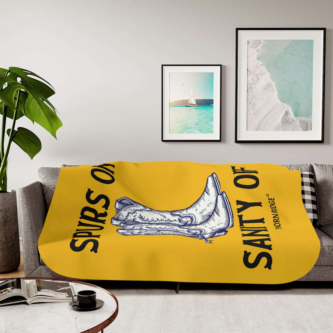 Spurs On Sanity Off yellow sherpa blanket with an illustration of white cowboy boots with spurs in the middle and branding Thorn Ridge®