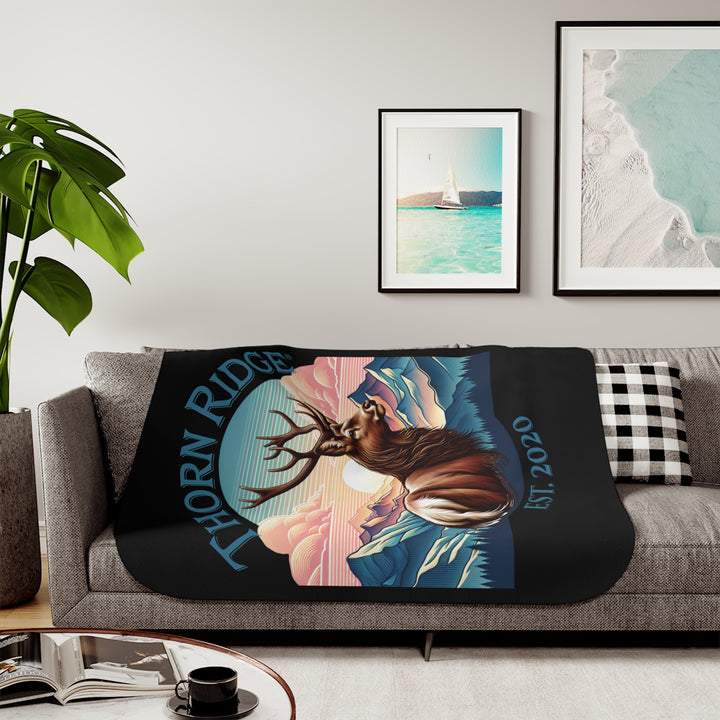 Black sherpa blanket with an illustration of a buck with antlers looking to the right with images of mountains in the background and the text Thorn Ridge® Est. 2020