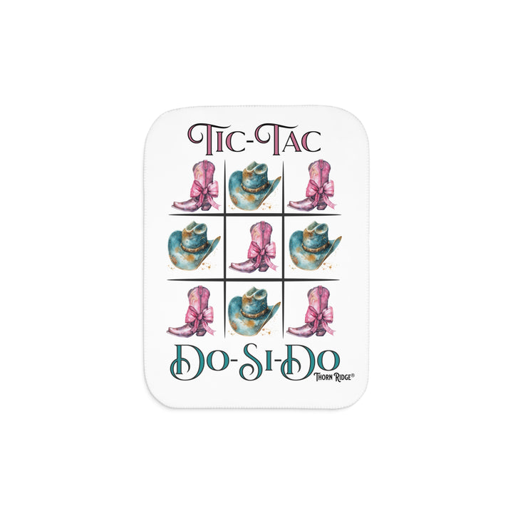 White Sherpa Blanket with a Tic-Tac Do-Si-Do image of a tic-tac-toe board with pink cowboy boots with a bow in the four corners and middle and blue cowboy hats on the sides by Thorn Ridge®