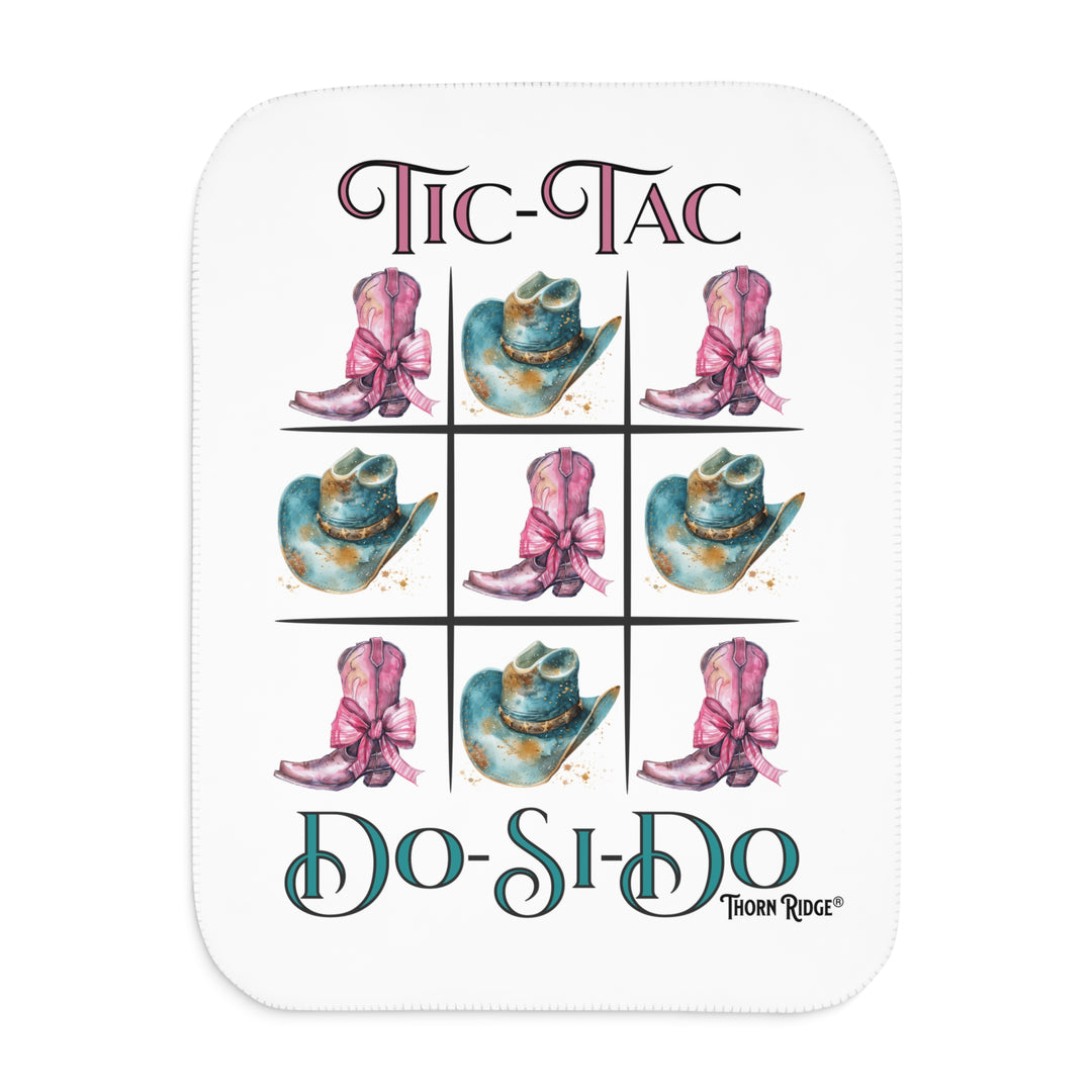 White Sherpa Blanket with a Tic-Tac Do-Si-Do image of a tic-tac-toe board with pink cowboy boots with a bow in the four corners and middle and blue cowboy hats on the sides by Thorn Ridge®