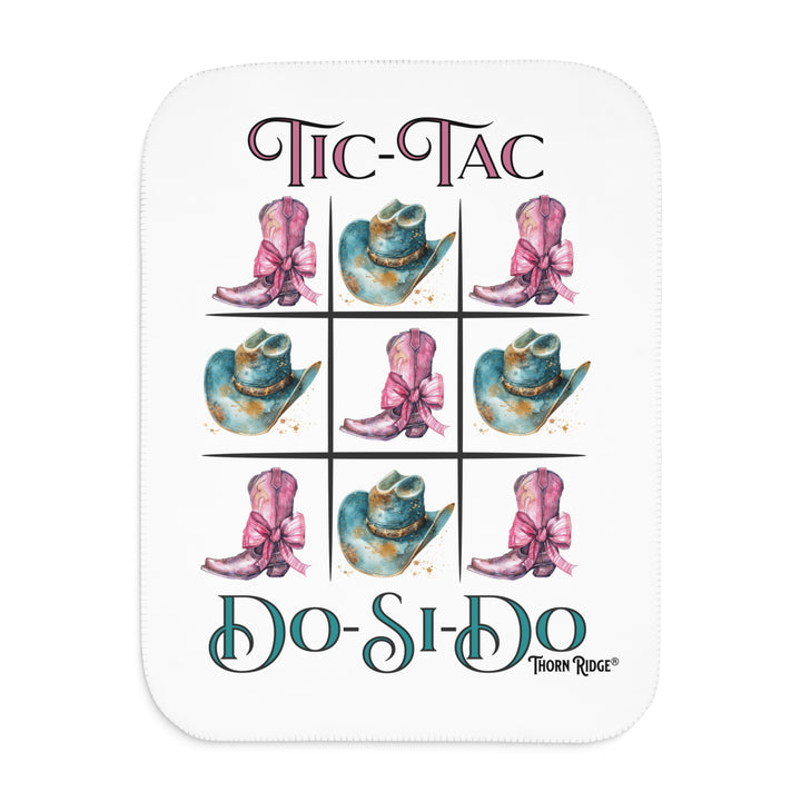 White Sherpa Blanket with a Tic-Tac Do-Si-Do image of a tic-tac-toe board with pink cowboy boots with a bow in the four corners and middle and blue cowboy hats on the sides by Thorn Ridge®