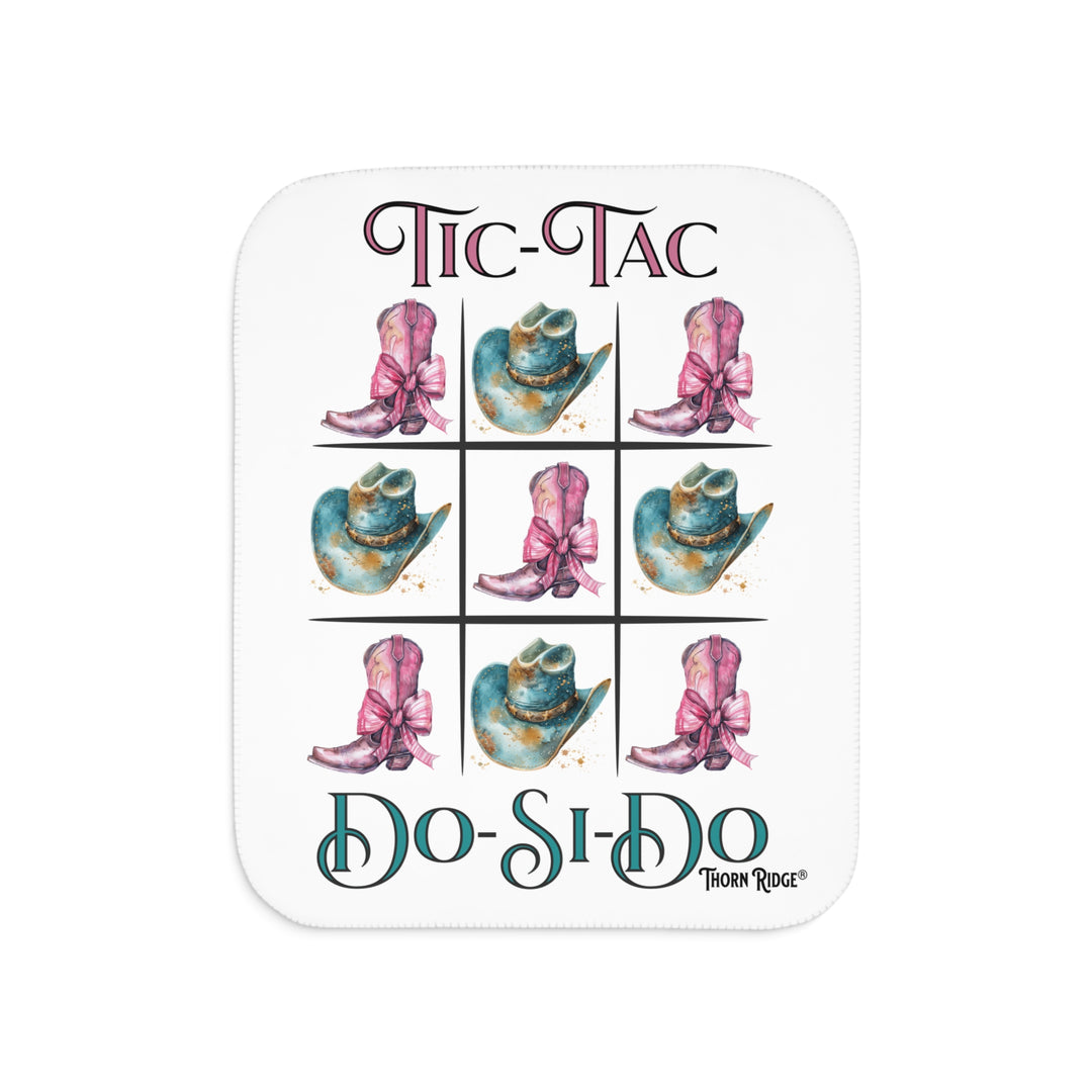 White Sherpa Blanket with a Tic-Tac Do-Si-Do image of a tic-tac-toe board with pink cowboy boots with a bow in the four corners and middle and blue cowboy hats on the sides by Thorn Ridge®
