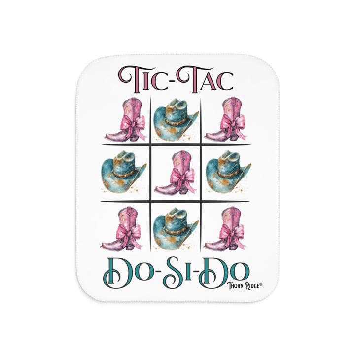 White Sherpa Blanket with a Tic-Tac Do-Si-Do image of a tic-tac-toe board with pink cowboy boots with a bow in the four corners and middle and blue cowboy hats on the sides by Thorn Ridge®