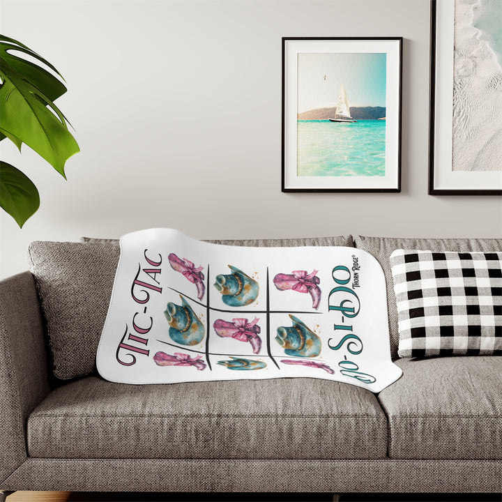 White Sherpa Blanket with a Tic-Tac Do-Si-Do image of a tic-tac-toe board with pink cowboy boots with a bow in the four corners and middle and blue cowboy hats on the sides by Thorn Ridge®