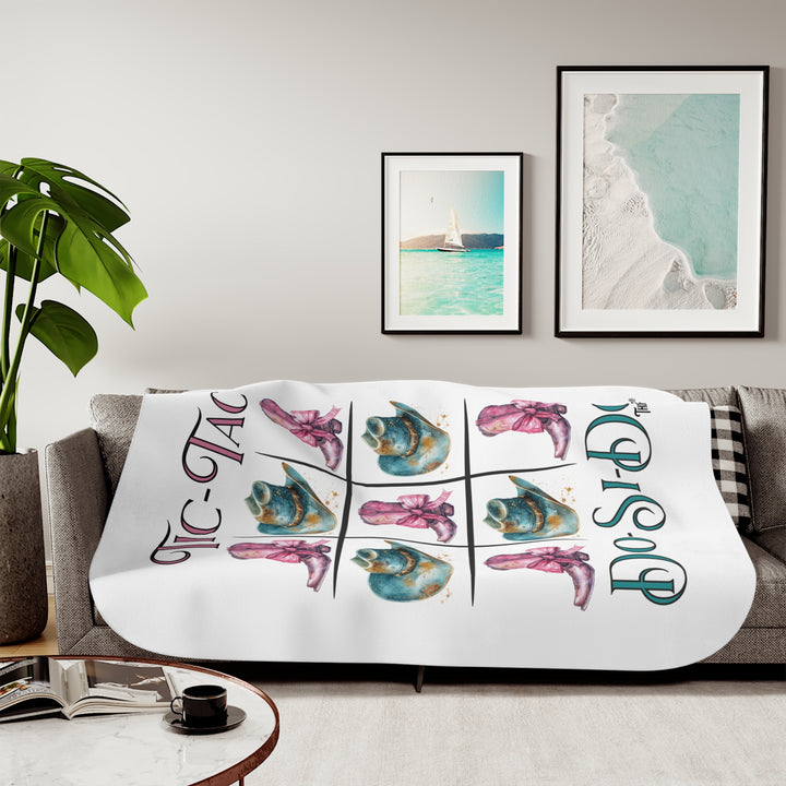 White Sherpa Blanket with a Tic-Tac Do-Si-Do image of a tic-tac-toe board with pink cowboy boots with a bow in the four corners and middle and blue cowboy hats on the sides by Thorn Ridge®