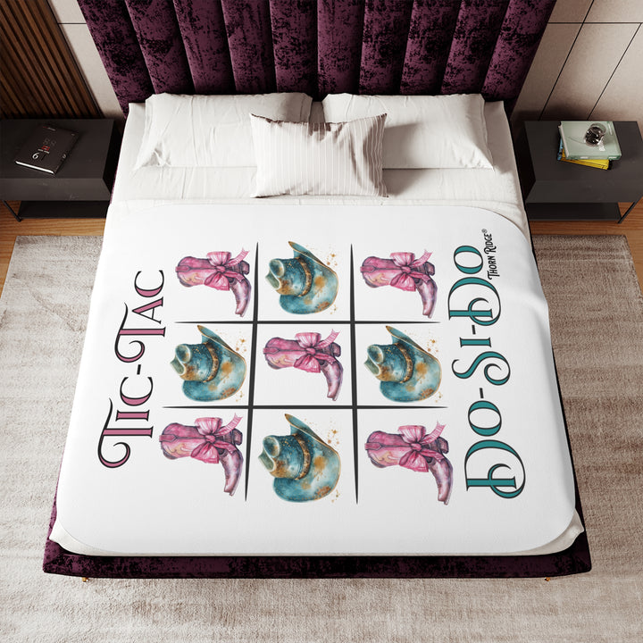 White Sherpa Blanket with a Tic-Tac Do-Si-Do image of a tic-tac-toe board with pink cowboy boots with a bow in the four corners and middle and blue cowboy hats on the sides by Thorn Ridge®