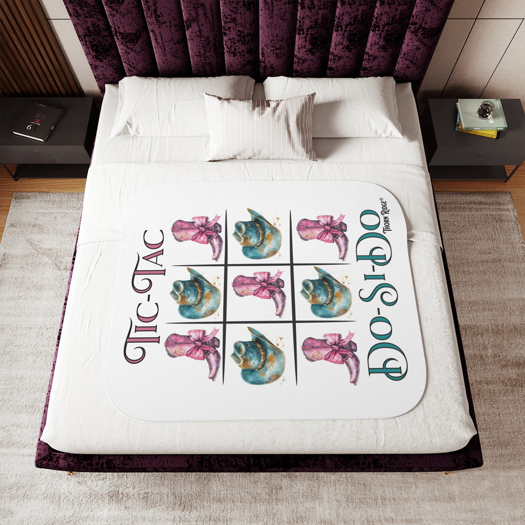 White Sherpa Blanket with a Tic-Tac Do-Si-Do image of a tic-tac-toe board with pink cowboy boots with a bow in the four corners and middle and blue cowboy hats on the sides by Thorn Ridge®