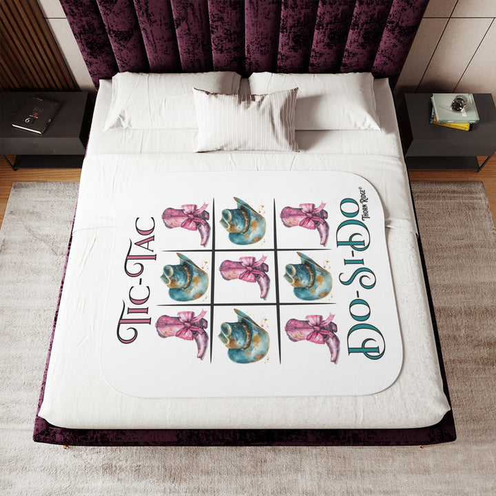 White Sherpa Blanket with a Tic-Tac Do-Si-Do image of a tic-tac-toe board with pink cowboy boots with a bow in the four corners and middle and blue cowboy hats on the sides by Thorn Ridge®