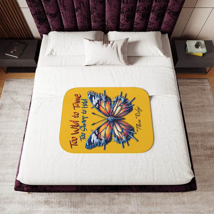 Butterfly design with barbed wire it's wings on a yellow sherpa blanket with text that says Too Wild to Tame Too Sharp to Hold and is the Barbfly legend from Thorn Ridge®