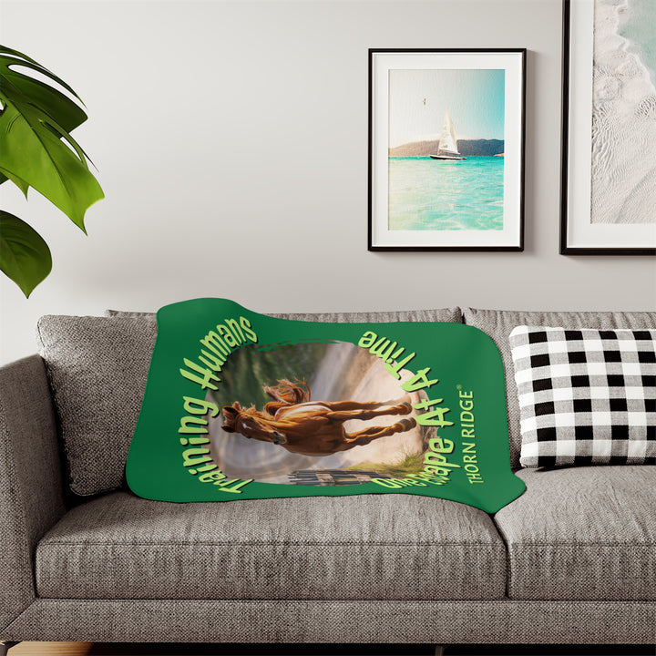 Training Humans One Escape At A Time  green sherpa blanket with the image of a bay horse running down a dirt road alongside a wooden fence. Labeled Thorn Ridge®
