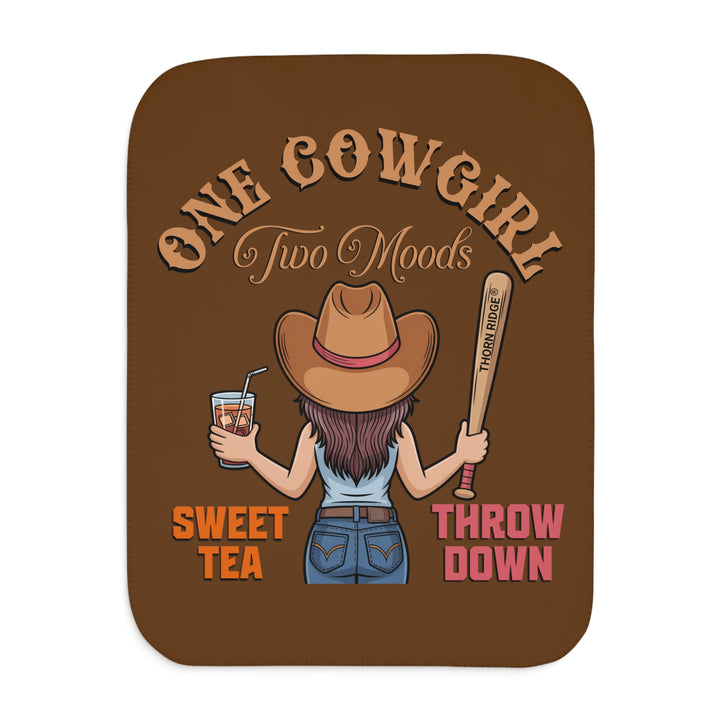 One Cowgirl Two Moods Sherpa Blanket by Thorn Ridge that's brown with a illustration of a cowgirl from the back holding a glass of sweet tea in the left hand and a baseball bat labeled Thorn Ridge® in the right hand with the words sweet tea under the glass and throw down under the bat. 