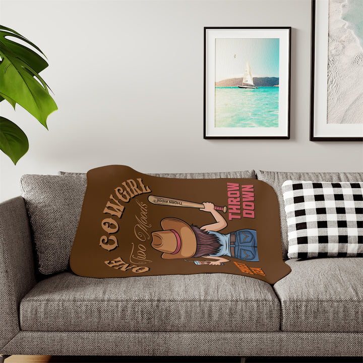 One Cowgirl Two Moods Sherpa Blanket by Thorn Ridge that's brown with a illustration of a cowgirl from the back holding a glass of sweet tea in the left hand and a baseball bat labeled Thorn Ridge® in the right hand with the words sweet tea under the glass and throw down under the bat. 