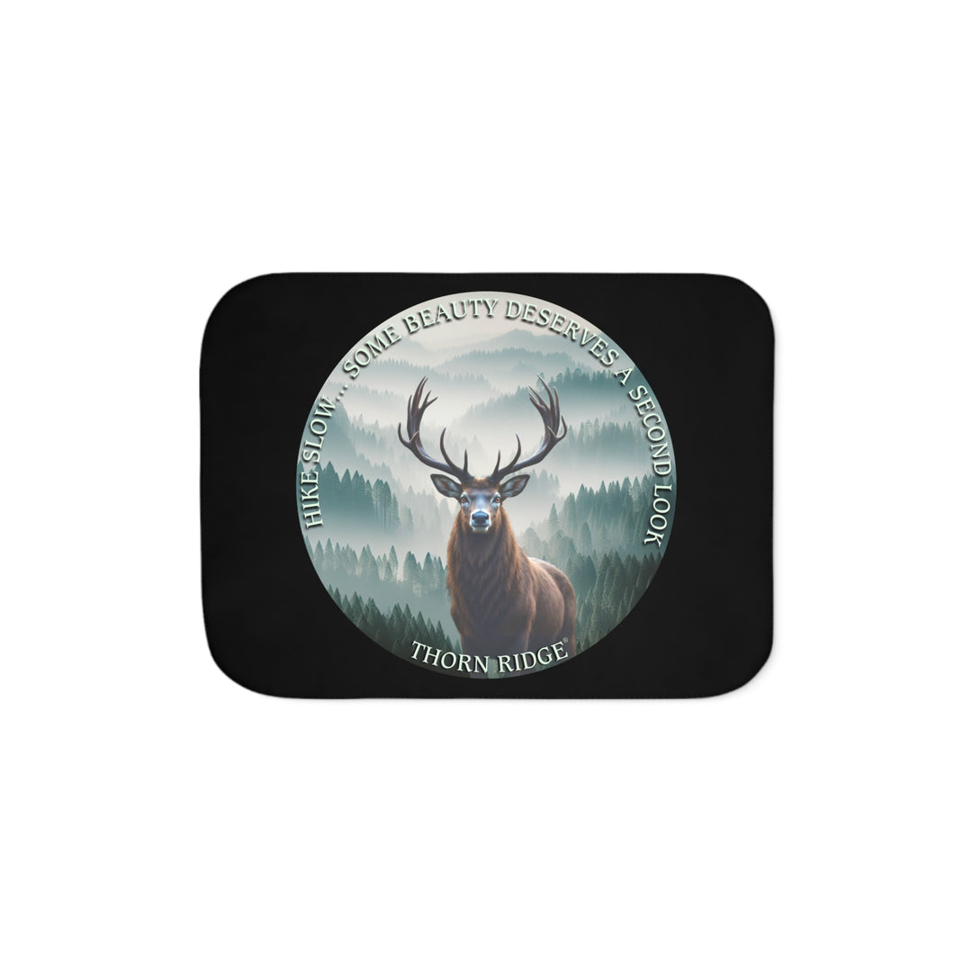 Hike Slow some beauty deserves a second look black sherpa blanket featuring a circular graphic of a buck looking at the camera with a green misty forest behind him and branded Thorn Ridge®