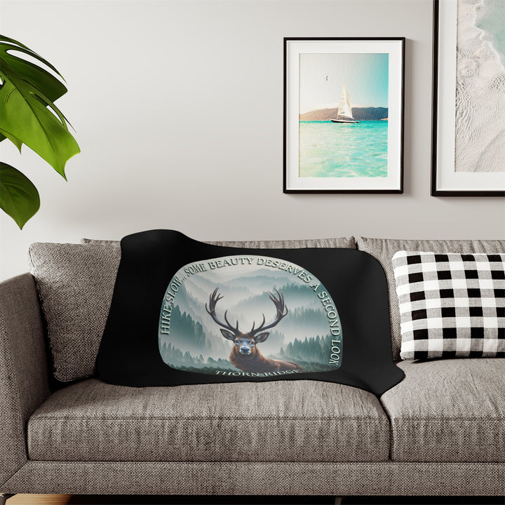 Hike Slow some beauty deserves a second look black sherpa blanket featuring a circular graphic of a buck looking at the camera with a green misty forest behind him and branded Thorn Ridge®