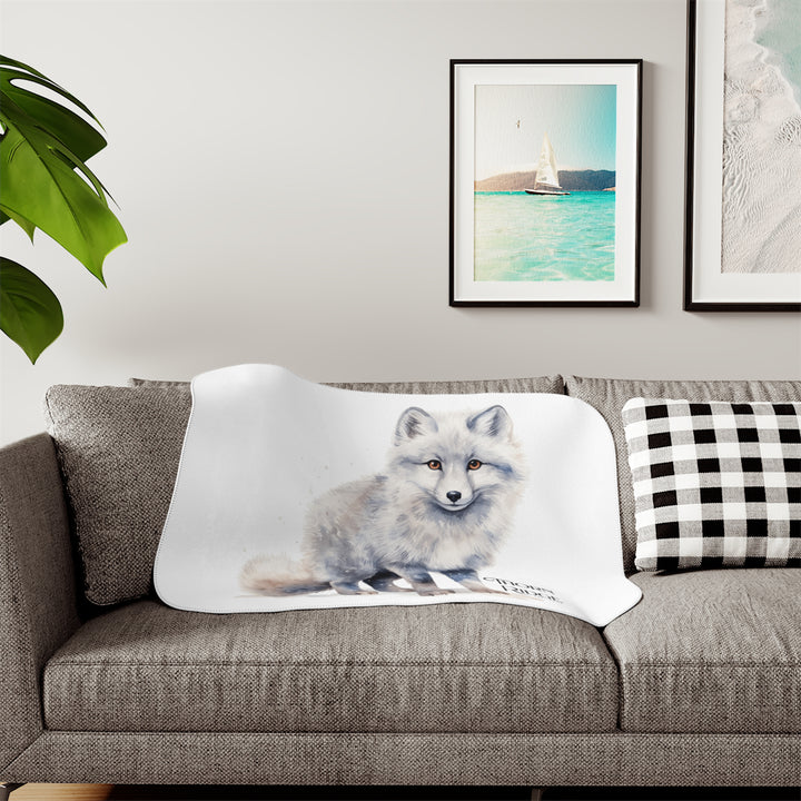 White Arctic fox illustration on a white Sherpa Blanket with 'Thorn Ridge' branding and the blanket is laying across a couch. 