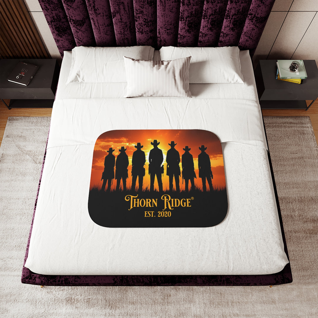 Silhouette of Seven Riders cowboys against an orange sunset with 'Thorn Ridge' branding on a sherpa blanket on a bed.
