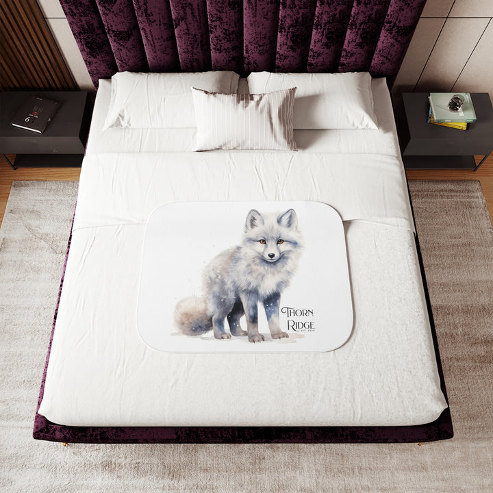 White Arctic fox illustration on a white Sherpa Blanket with 'Thorn Ridge' branding and the blanket is laying across a bed. 