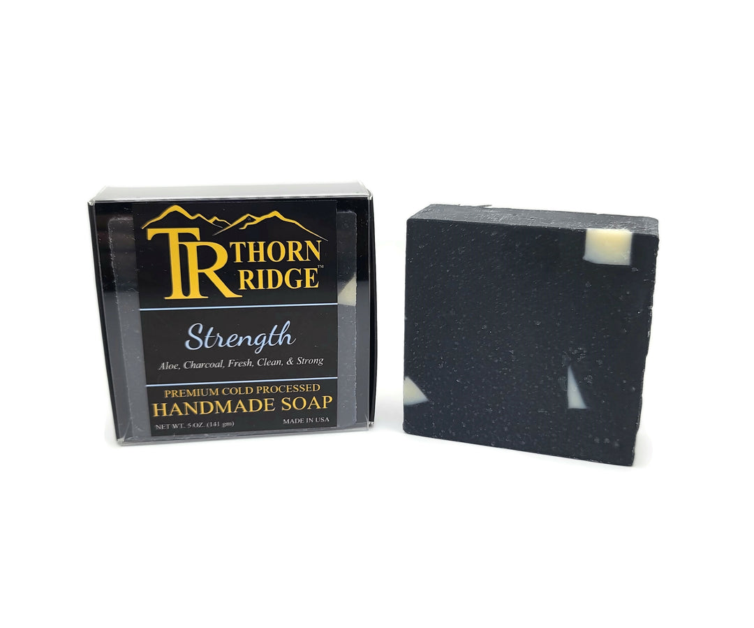 Packaging of Thorn Ridge soap labeled "Strength," described as aloe, charcoal, fresh, clean, and strong, premium cold processed, handmade, 5 oz. Made in USA.